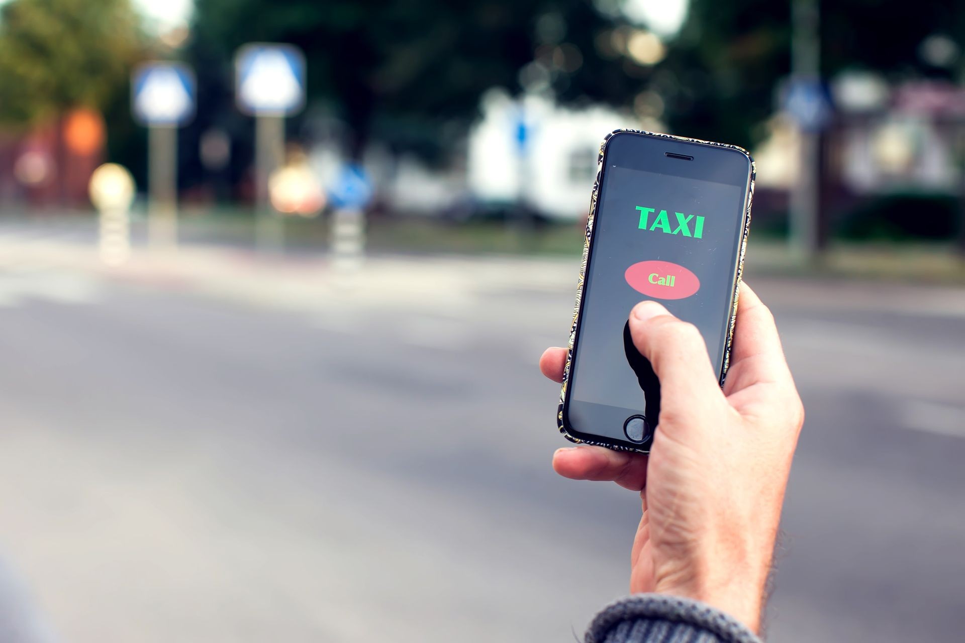 Male hand with smartphone on blurred road background. Taxi service application on the screen.